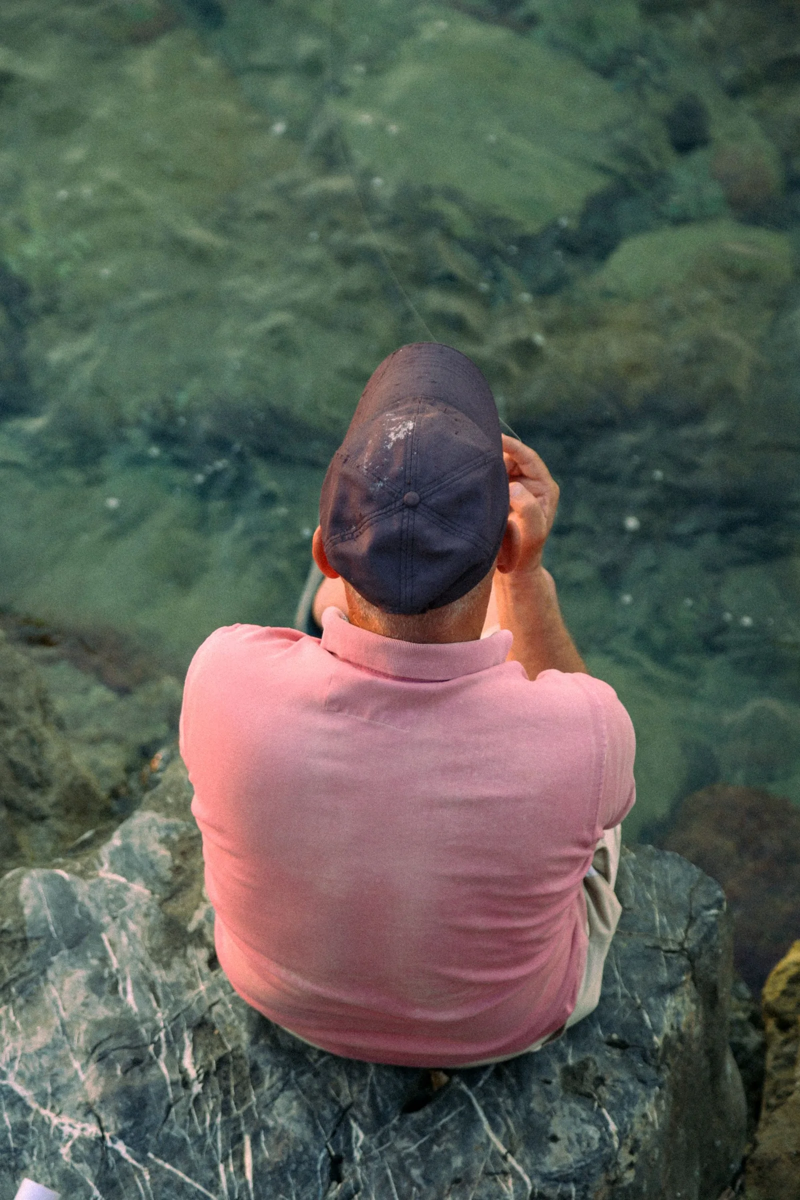 An angler in a pink shirt fishing from coastal rocks