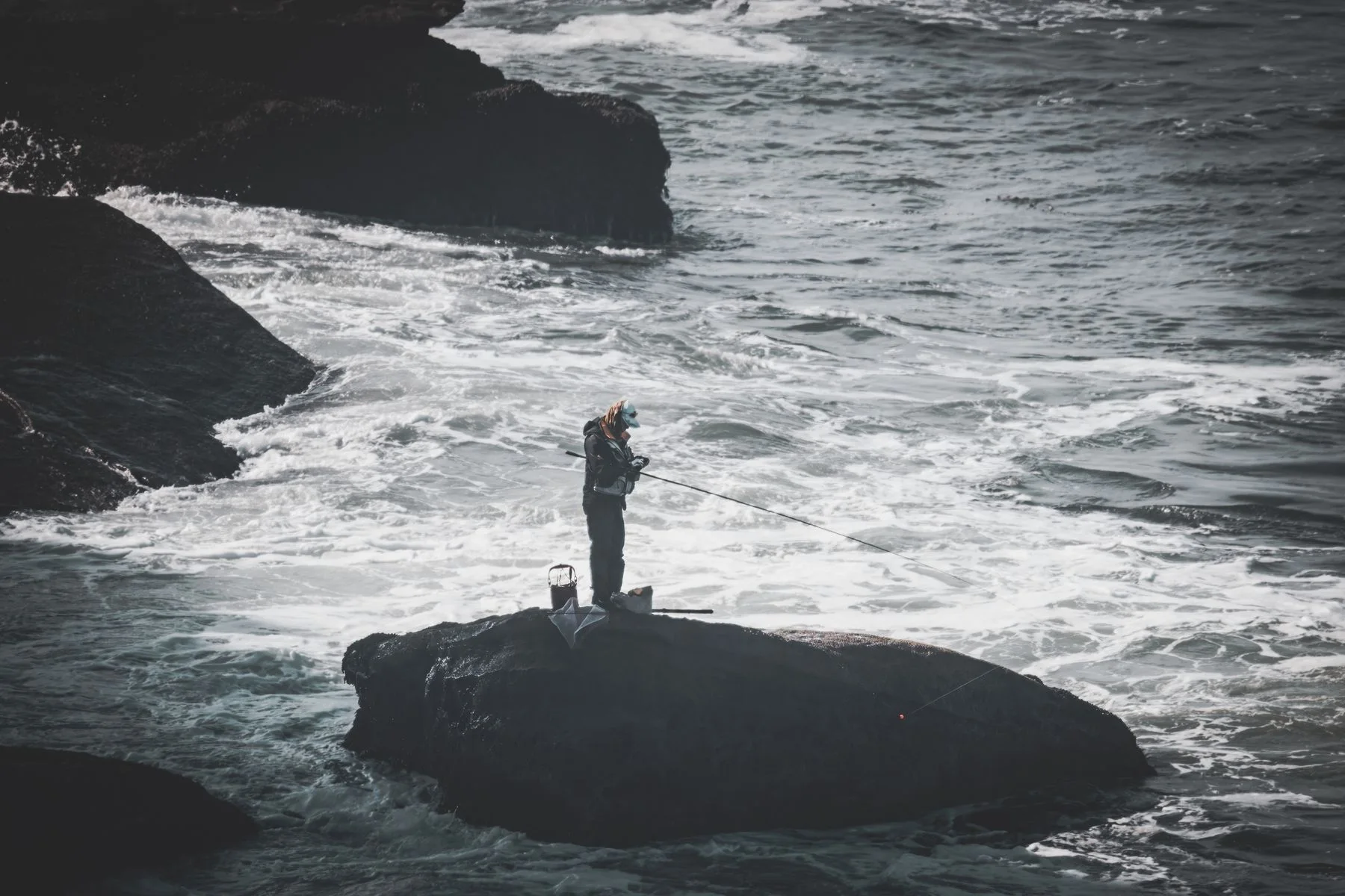 A lone angler beside rolling waves on a rocky shoreline
