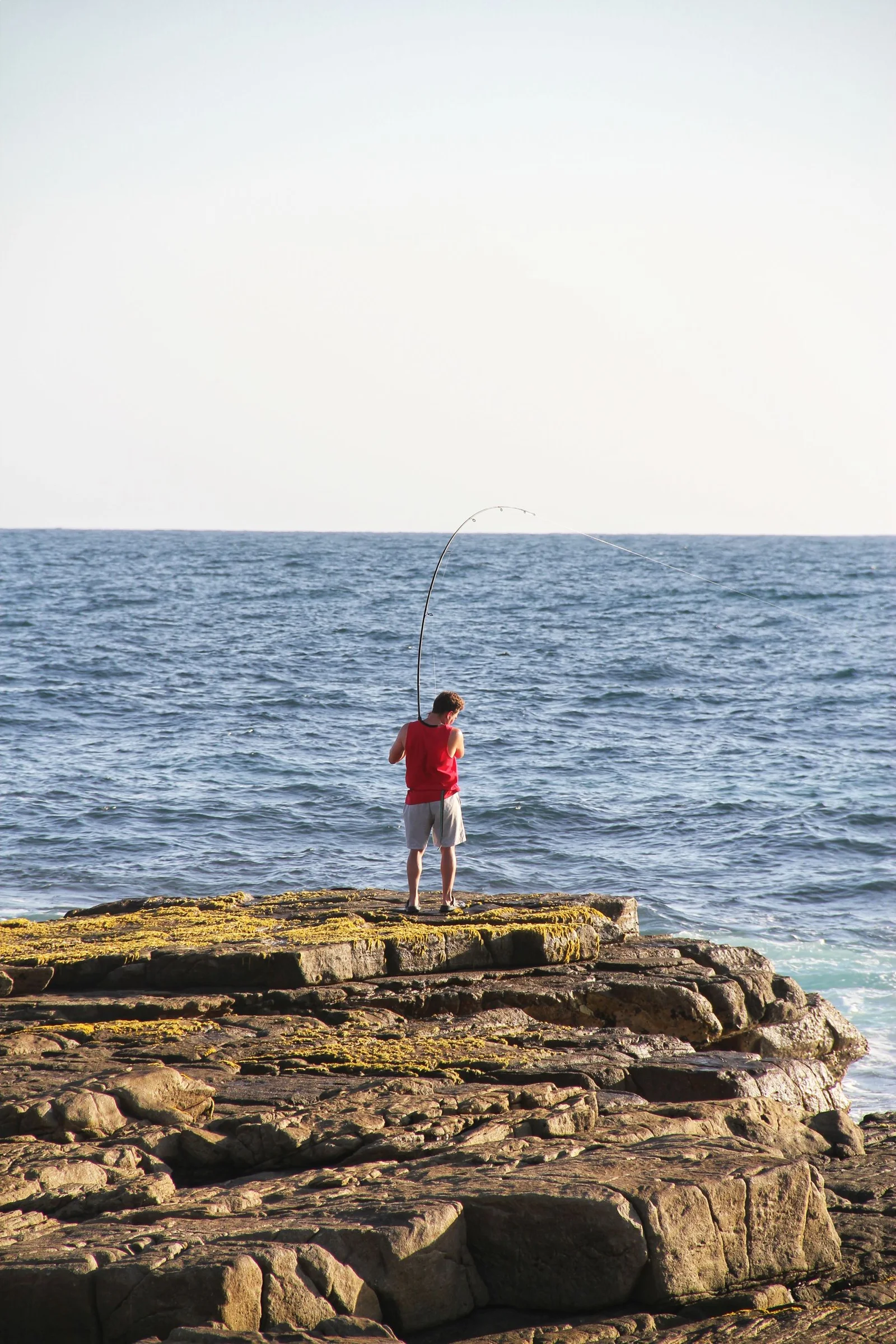 An angler in a red shirt casting from coastal rocks