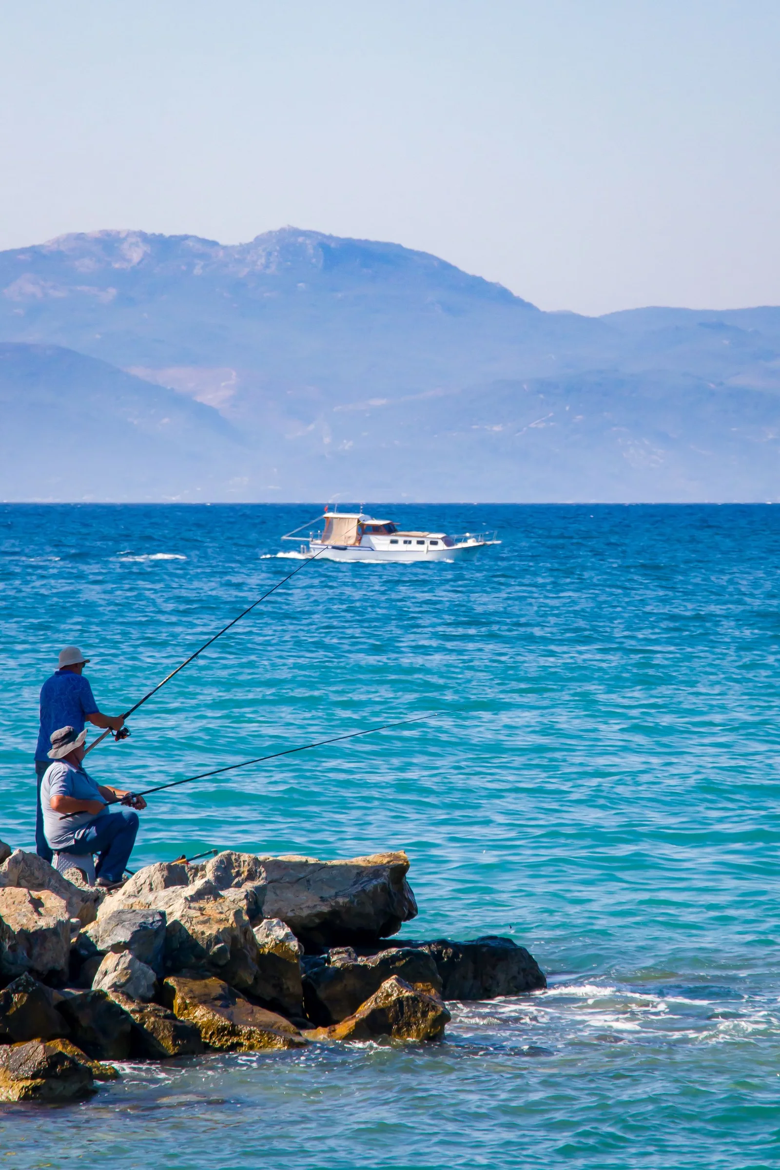 Two anglers beside the sea with hills in the distance